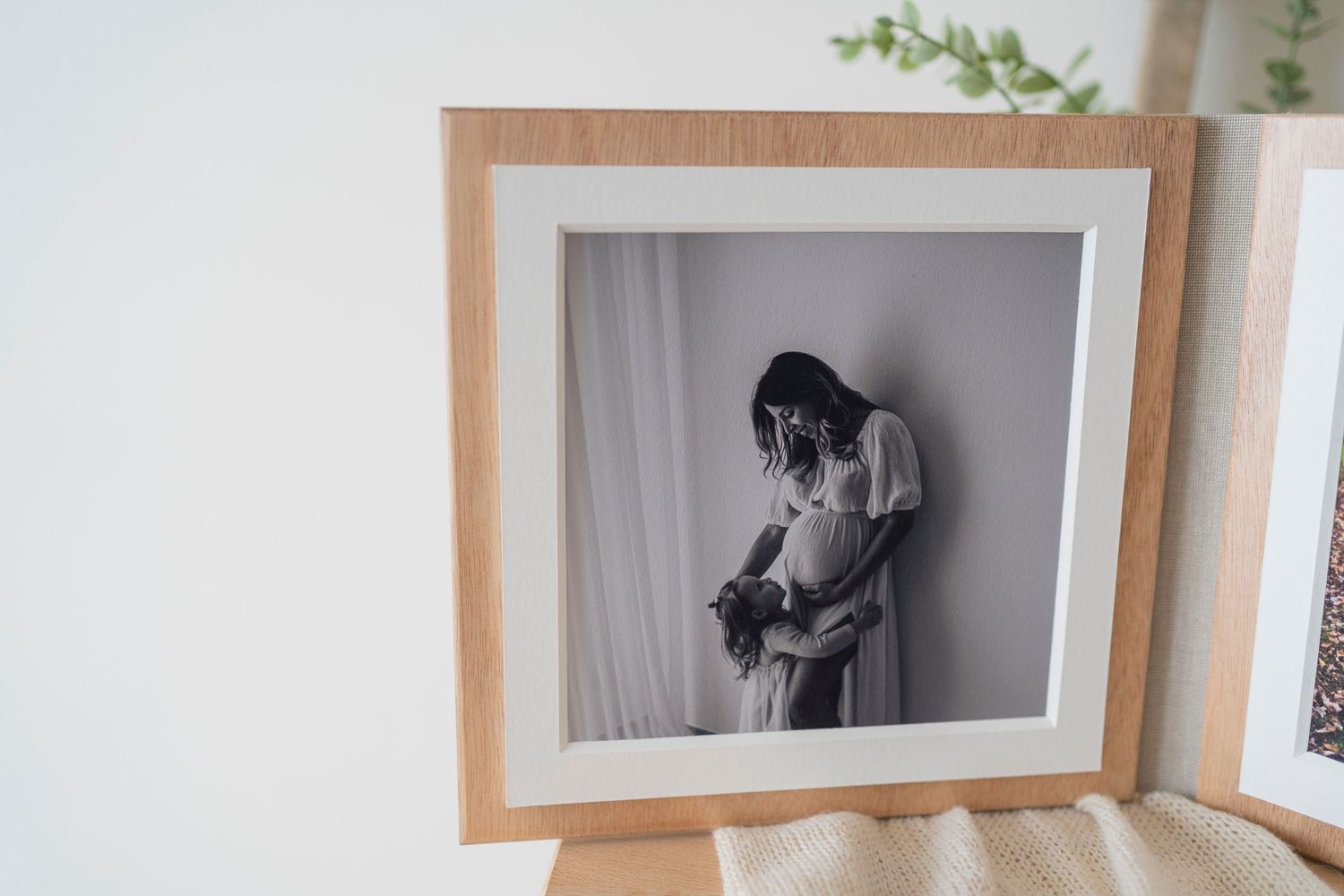 Black and white maternity portrait displayed in natural wood frame on white wall.