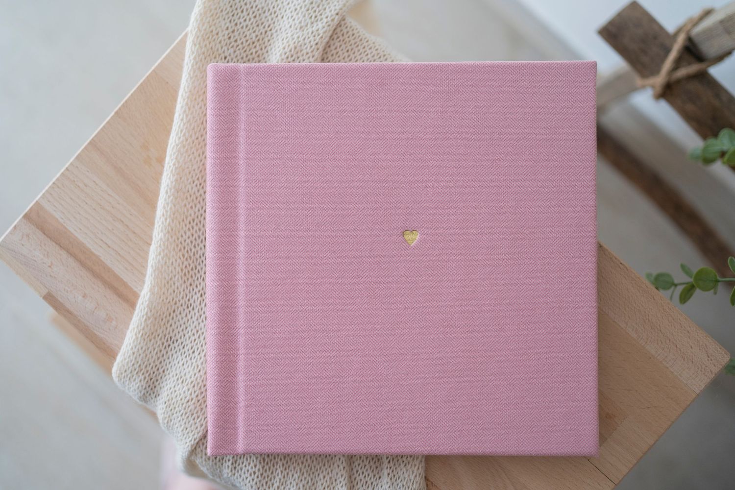 Pink linen hardcover photo album with gold heart detail on wooden surface.