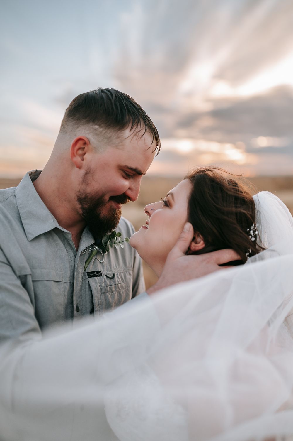 Romantic sunset wedding portrait with flowing veil and dramatic sky.
