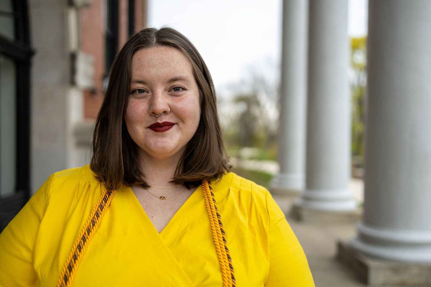 A person in a bright yellow dress smiling warmly in front of white columns.
