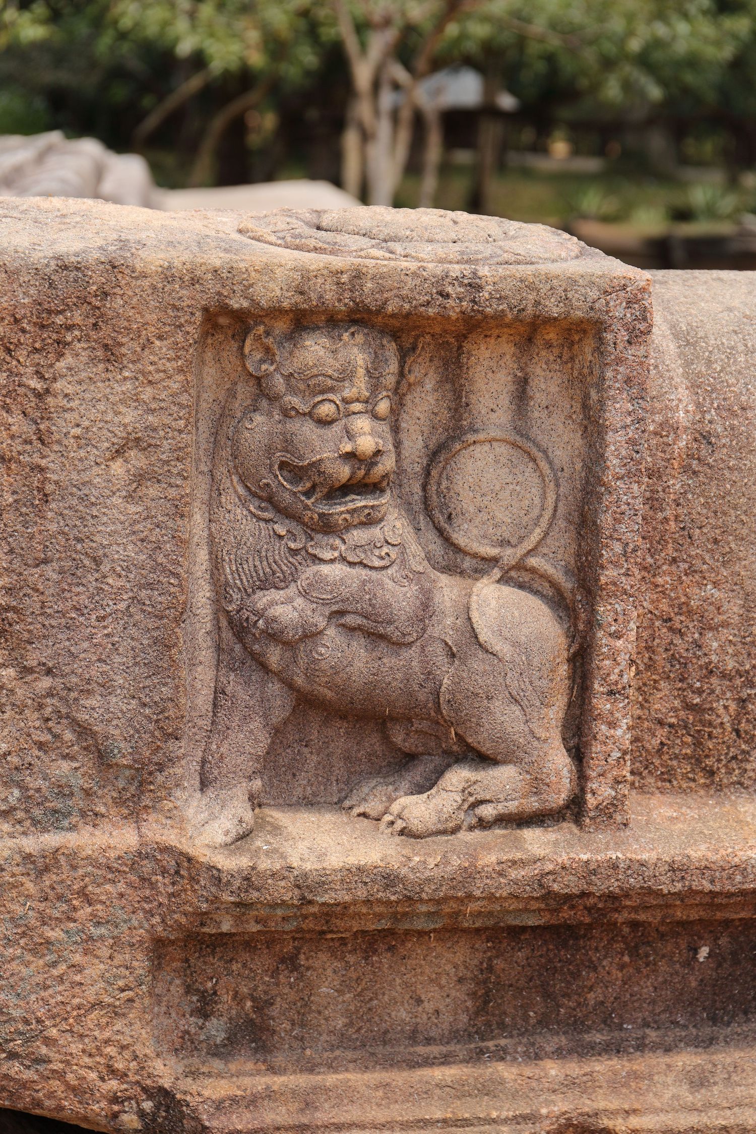 Ancient stone carving of a lion figure holding a decorative disc on temple wall.