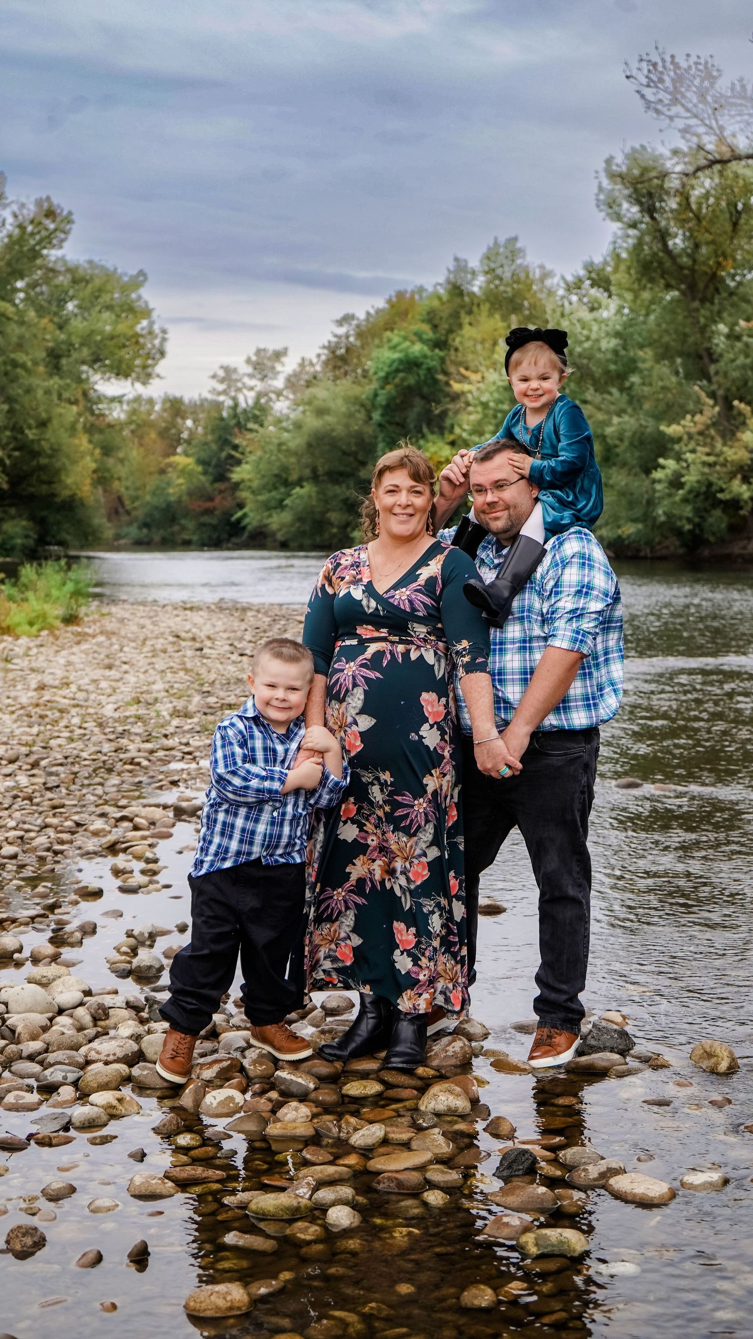 A family poses together on rocky riverbed with flowing water in the background.