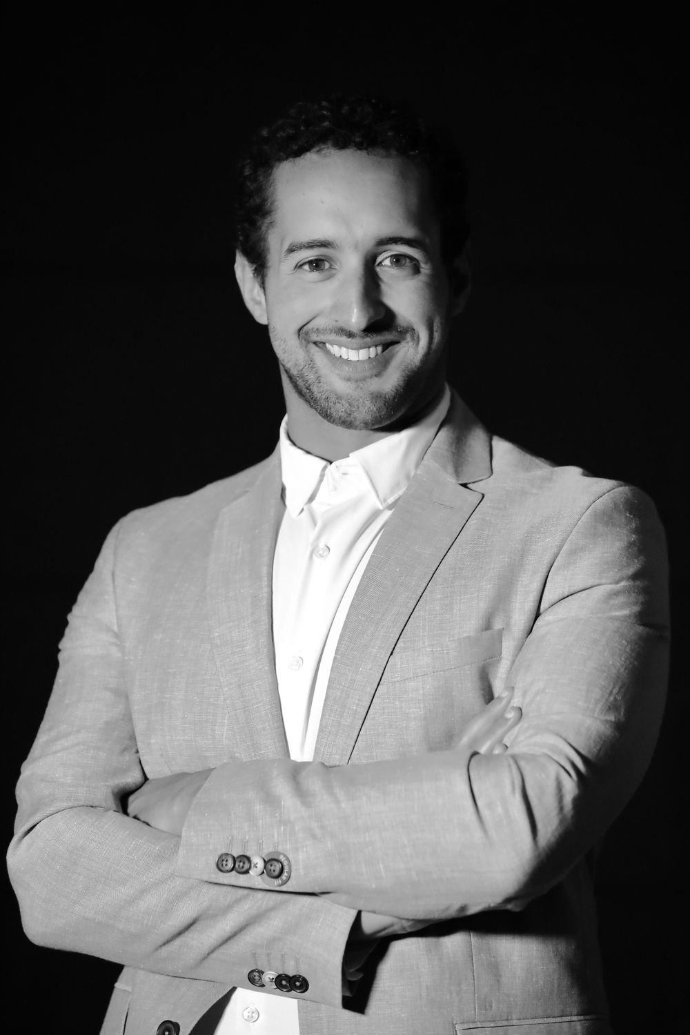 Professional black and white headshot of a man in a light colored suit smiling at the camera.