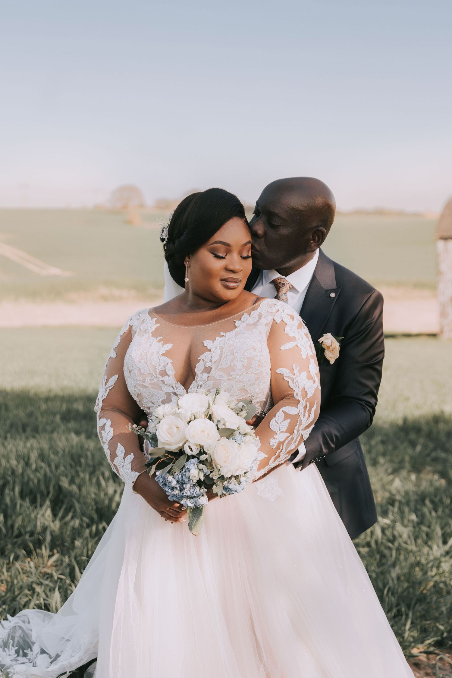 An intimate wedding portrait of a couple sharing a tender moment in a grassy field.
