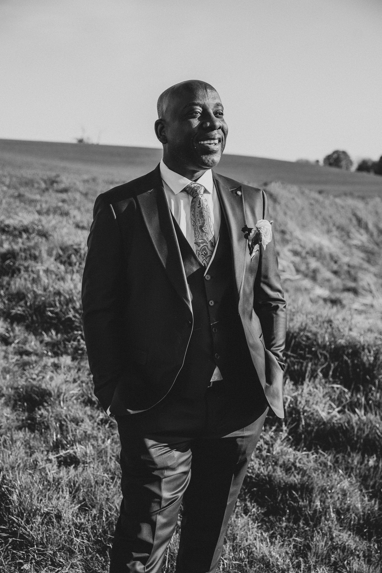 Black and white portraits of a groom in a formal suit posing in an outdoor setting.