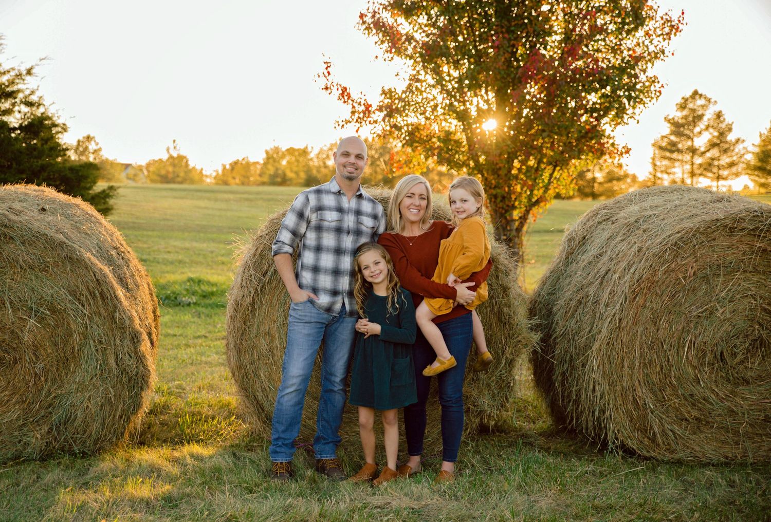 Family portrait session at sunset with hay bales in a rustic farm setting.