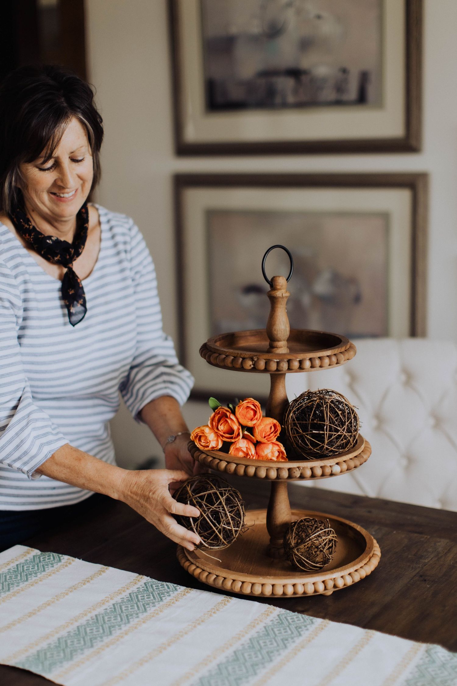 Decorative wooden tiered stand with orange roses and woven spheres on a table.