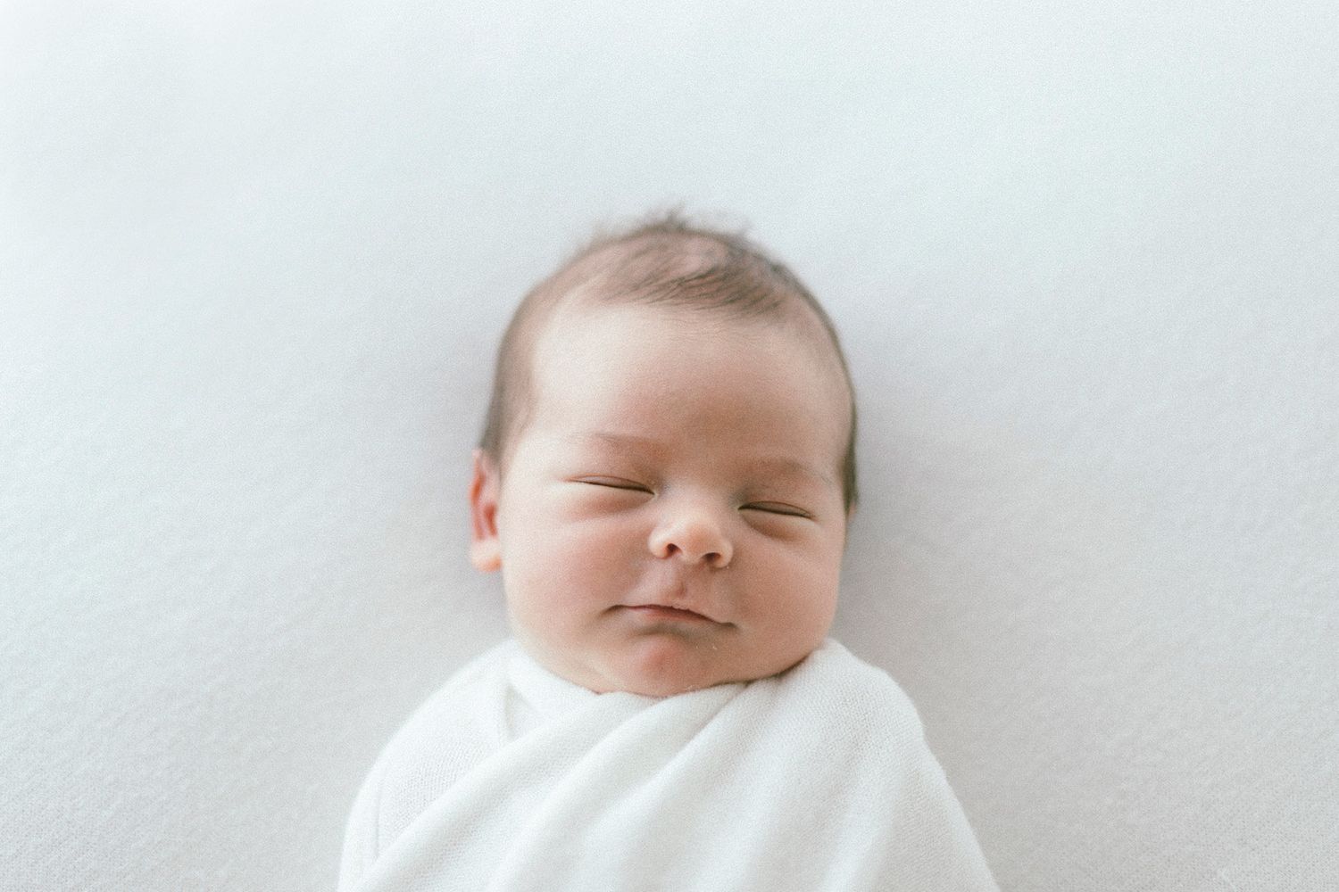 Peaceful newborn baby sleeping on white sheets with soft natural lighting.