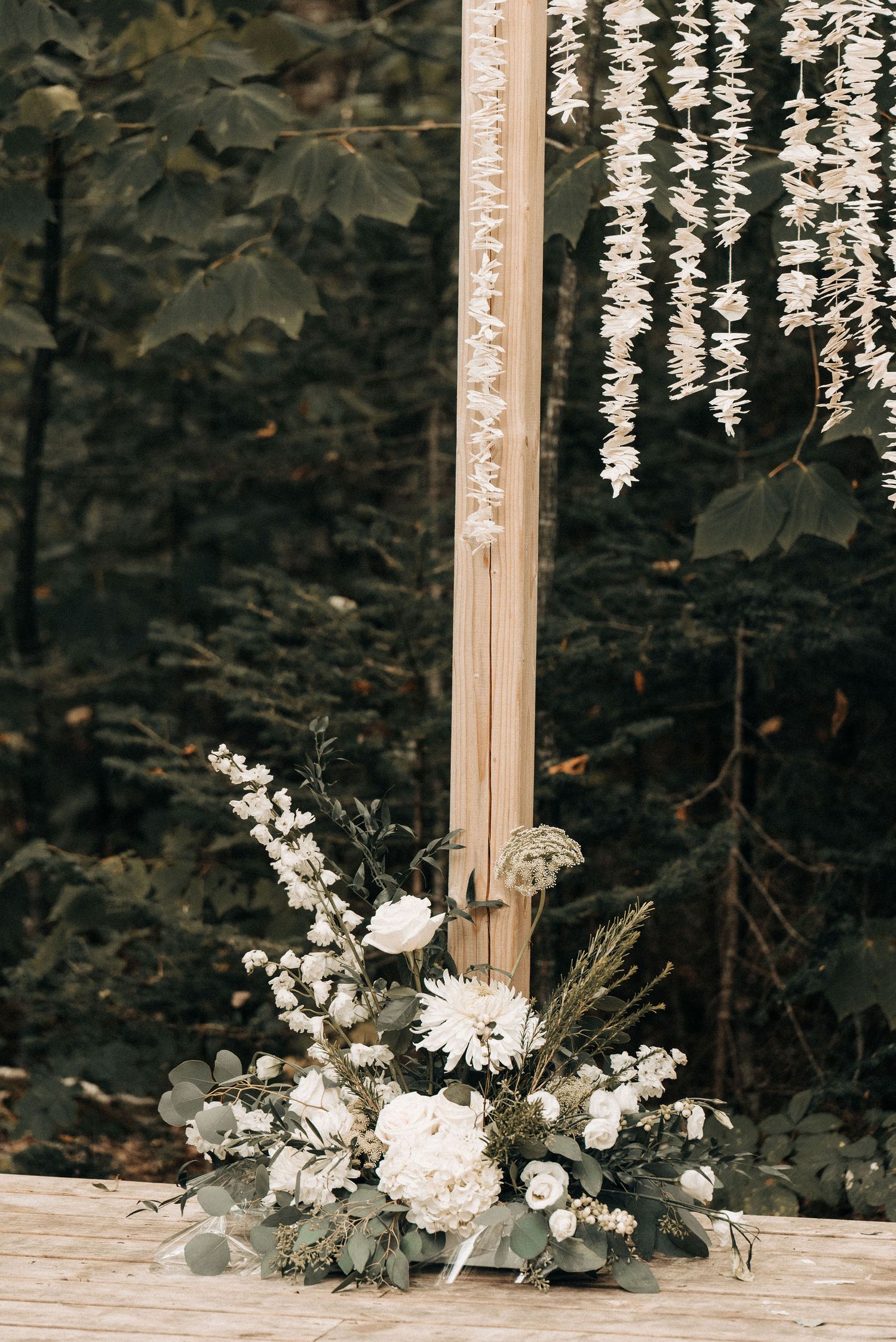 Elegant floral arrangement with cascading white decorations and fresh flowers on wooden posts.