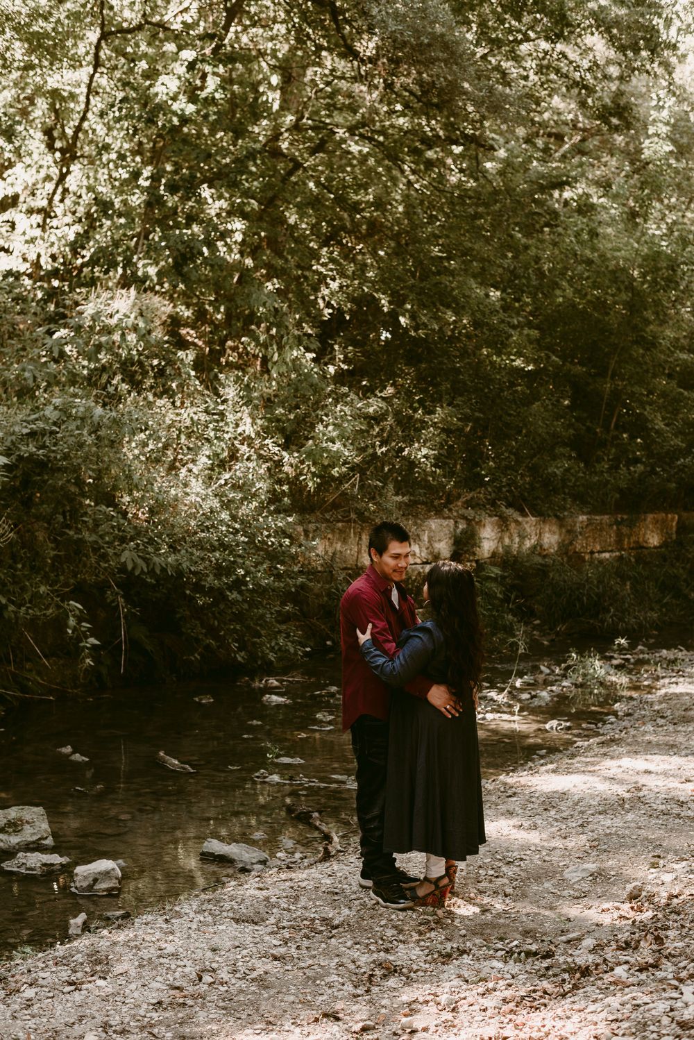 A couple in coordinated outfits shares a tender moment on a forest trail.