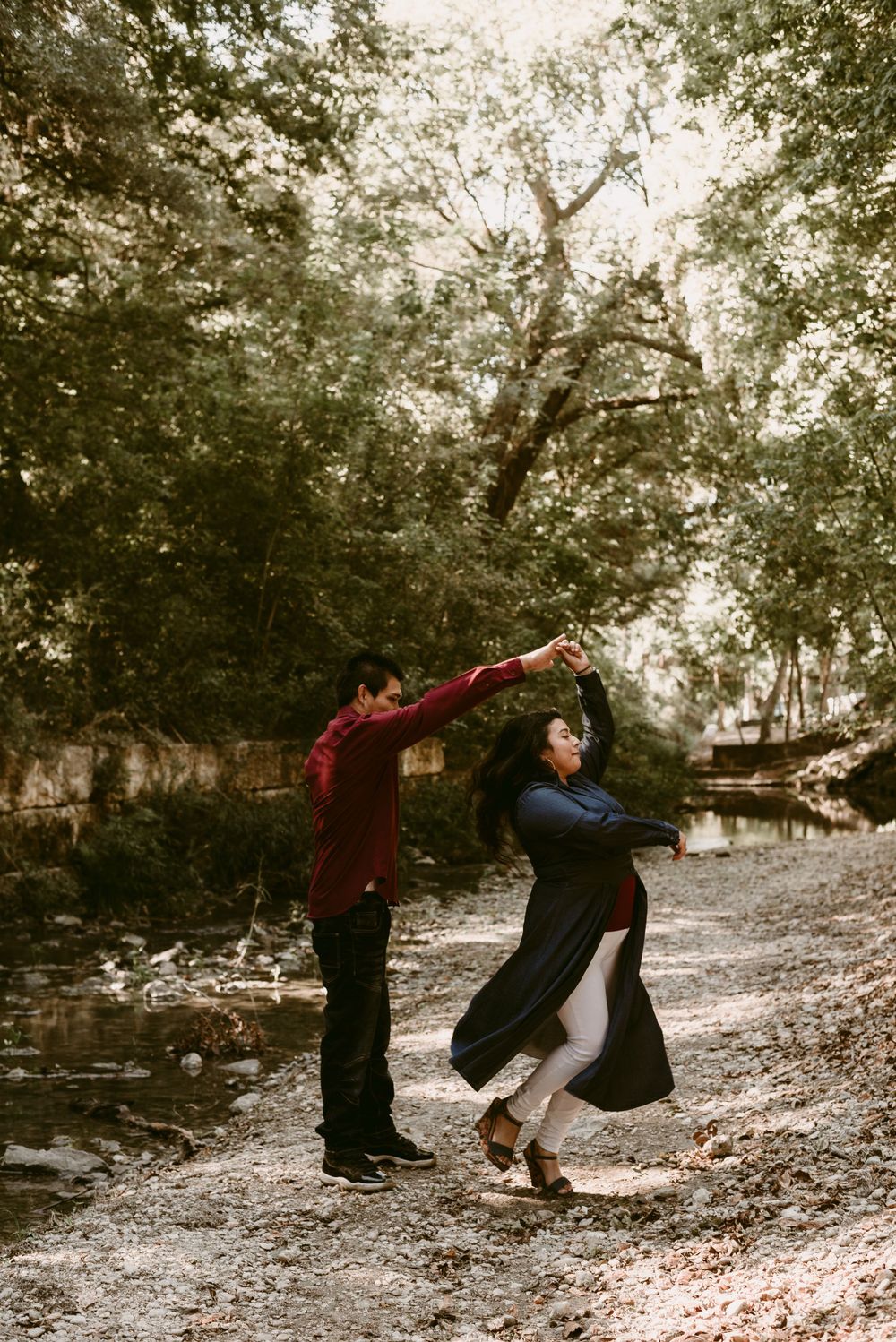 A couple performs a romantic dance move on a wooded path by a stream.
