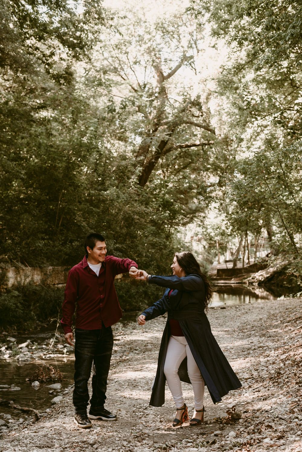 A couple dances playfully on a woodland path beside a stream in autumn.