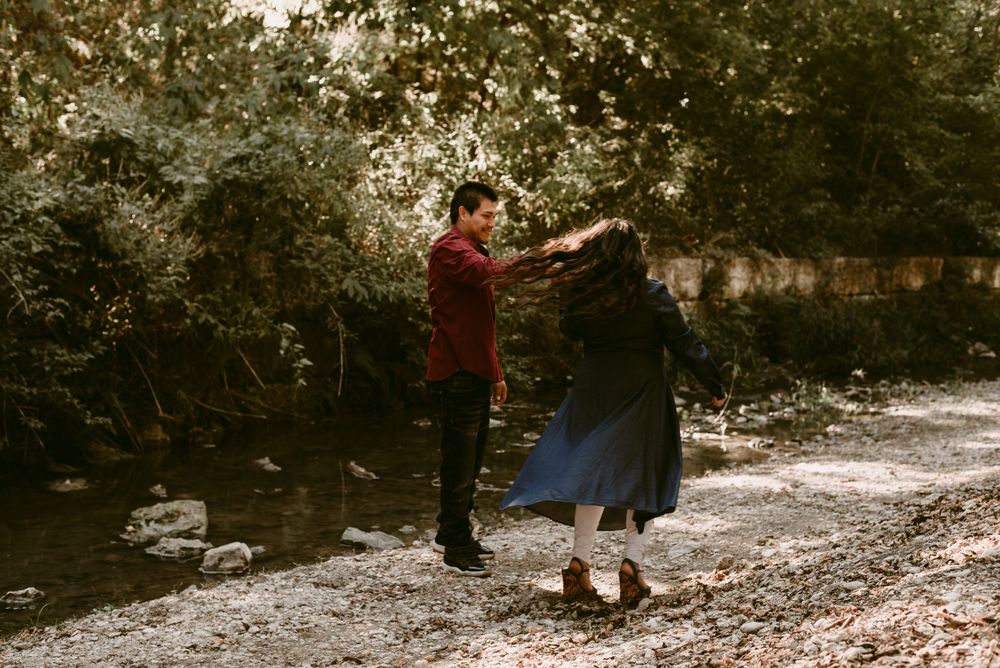 A dancing couple in burgundy and navy spins together on a scenic forest path.