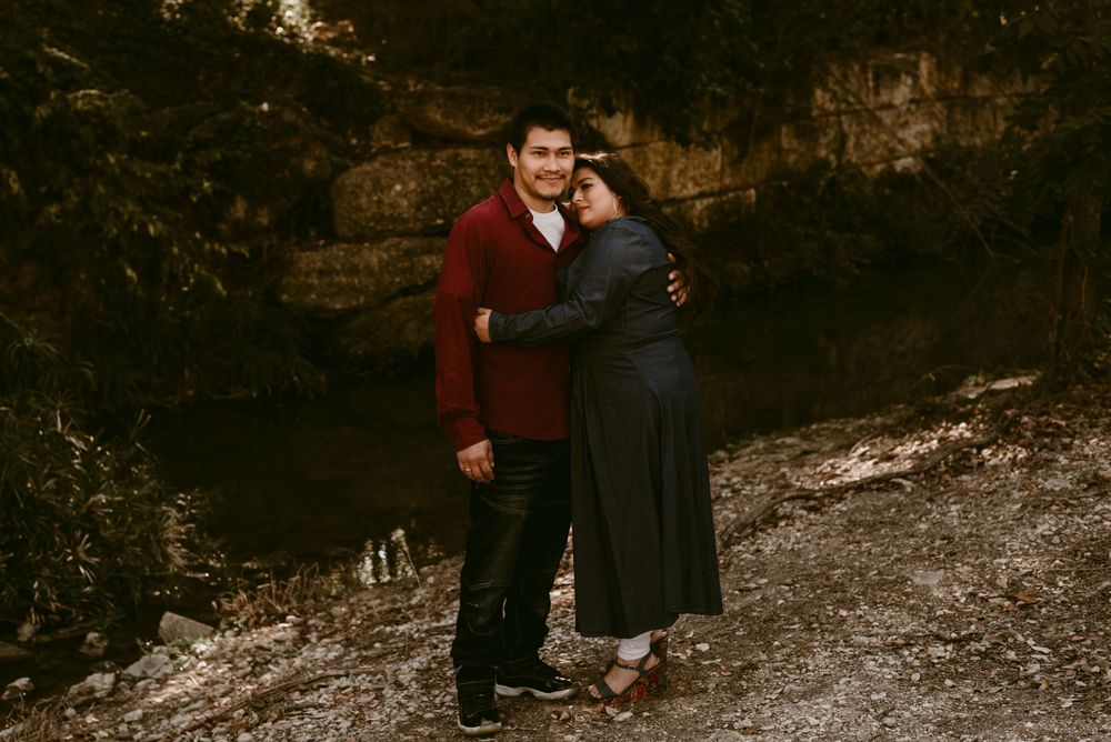 A couple embraces on a rocky path wearing burgundy and navy outfits during an autumn photoshoot.
