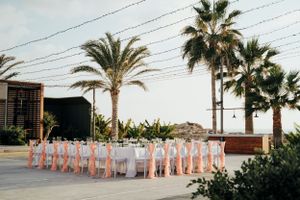 Pink chairs lined up for an outdoor wedding ceremony with palm trees and power lines in the background.