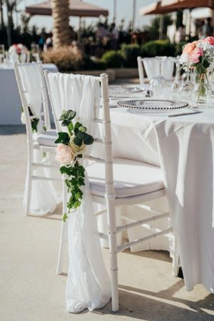 White chiavari chair decorated with flowing white fabric and roses at an outdoor wedding reception.