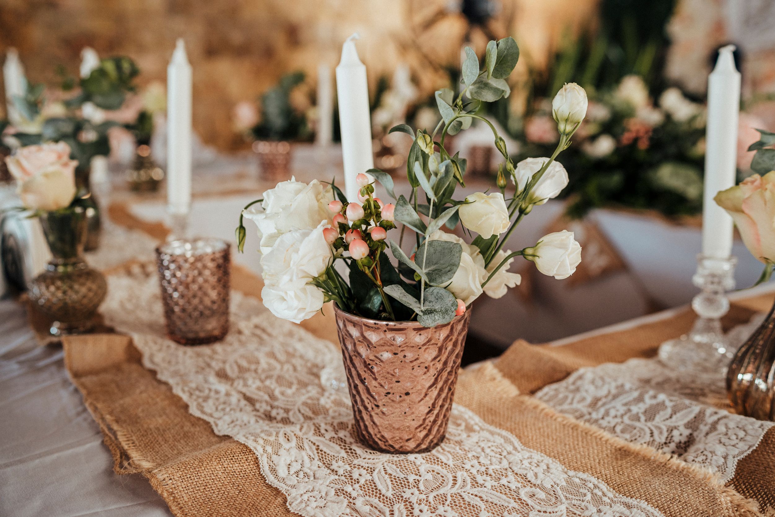 Vintage wedding table decor with rose gold votive holders, white flowers and lace runners.