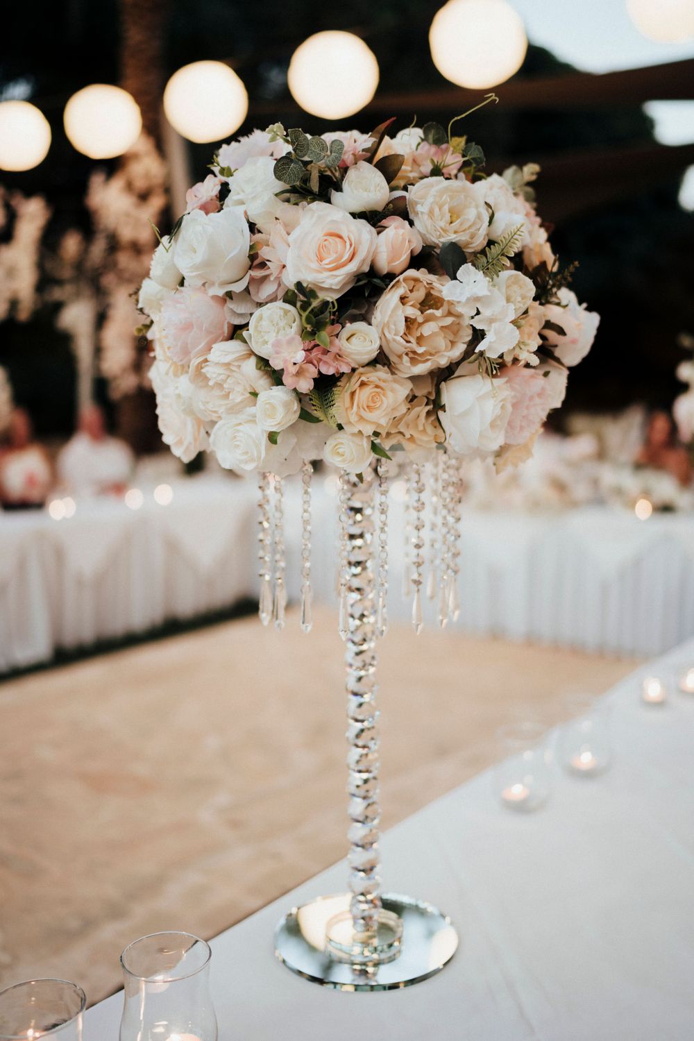 Crystal-adorned centerpiece featuring blush and white roses on a mirrored stand.