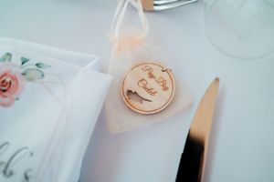 Wooden circular wedding favor with delicate floral details next to table settings.