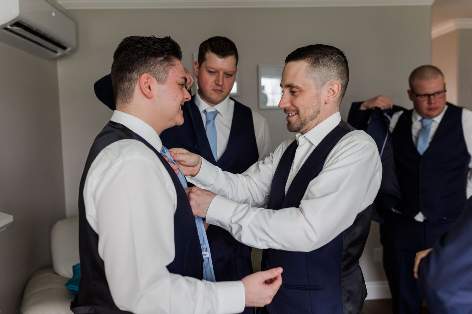 A group of men in formalwear help each other get ready before a wedding ceremony.