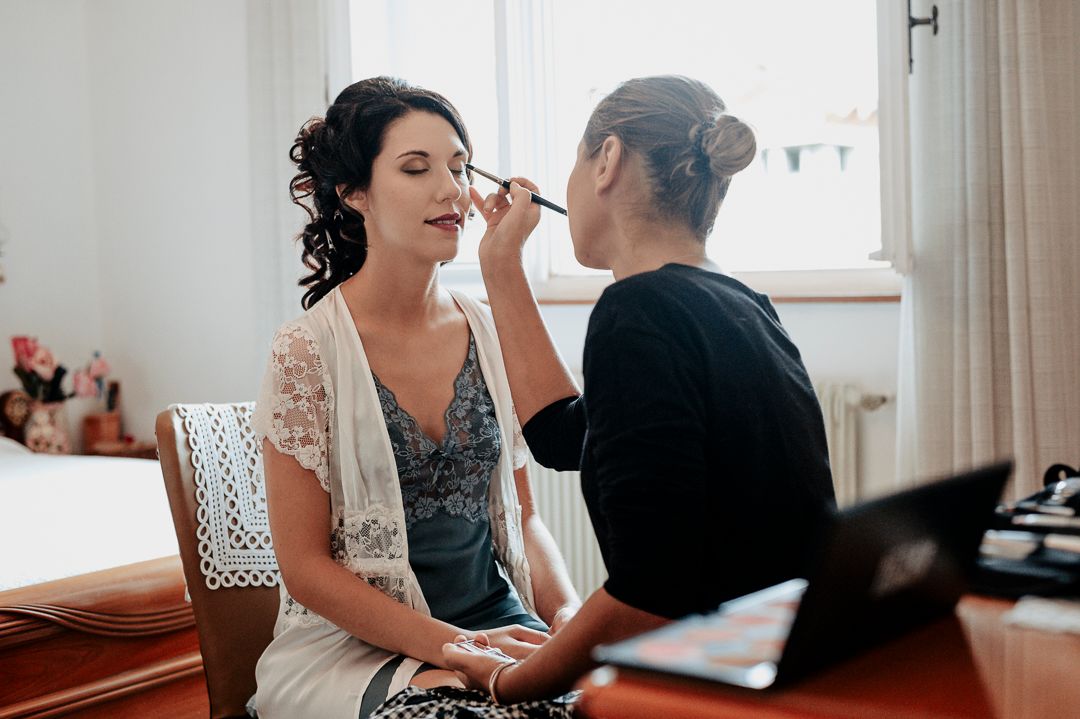 Behind the scenes wedding preparation with makeup artist working on bride.