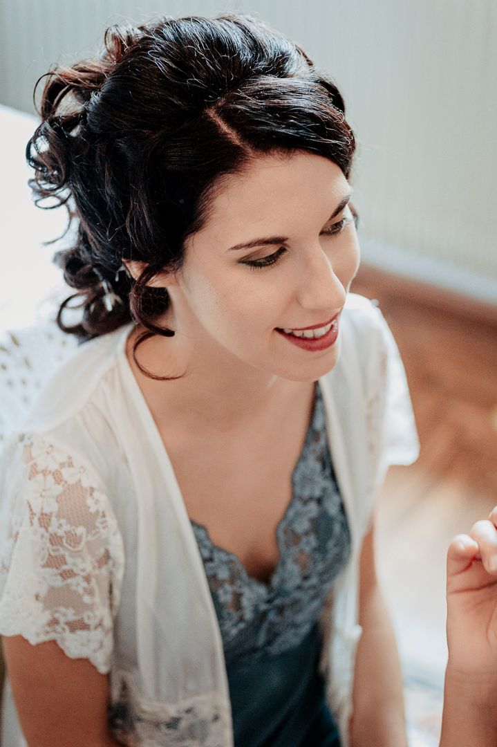 Bride getting ready with elegant updo hairstyle and lace robe.