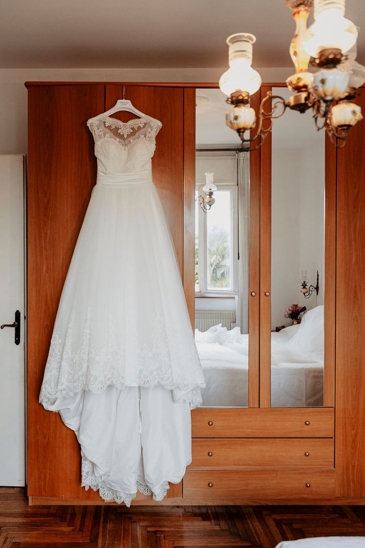 Classic white lace wedding dress hanging on wooden wardrobe with vintage lighting.
