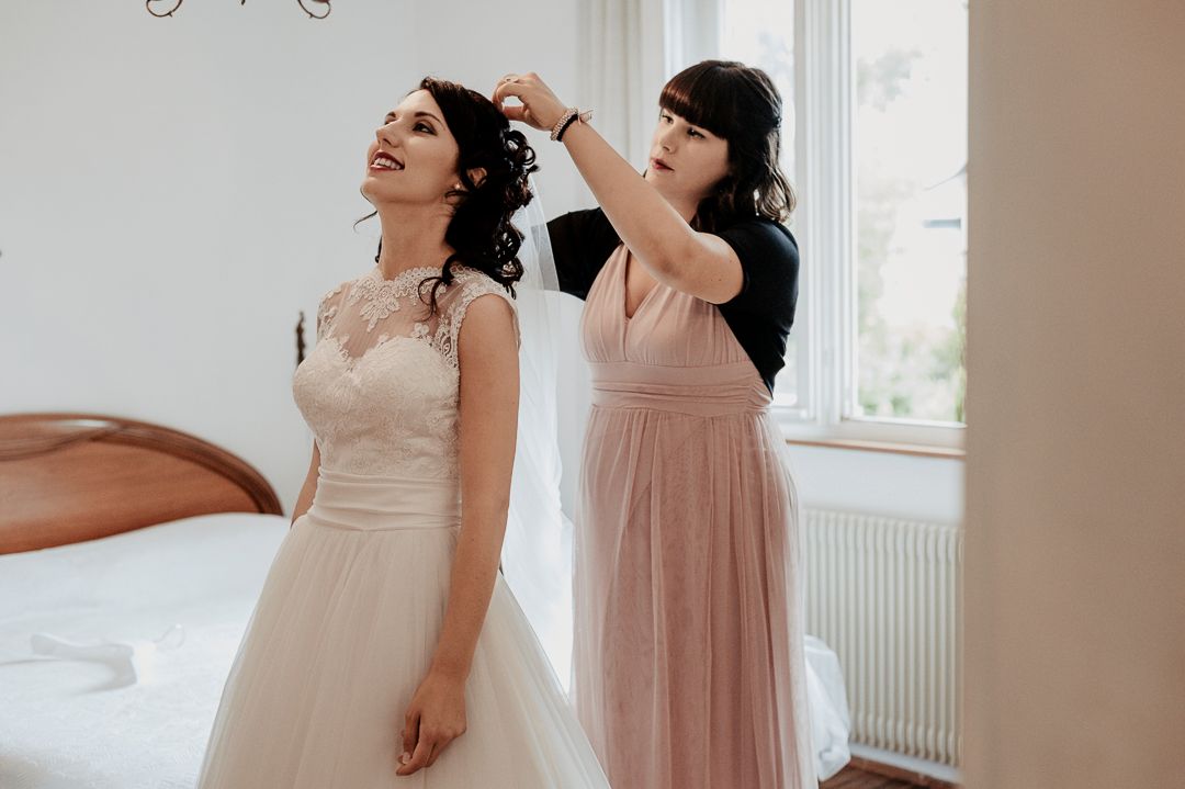 Final wedding preparations with hairstyling taking place in a bright sunlit room.