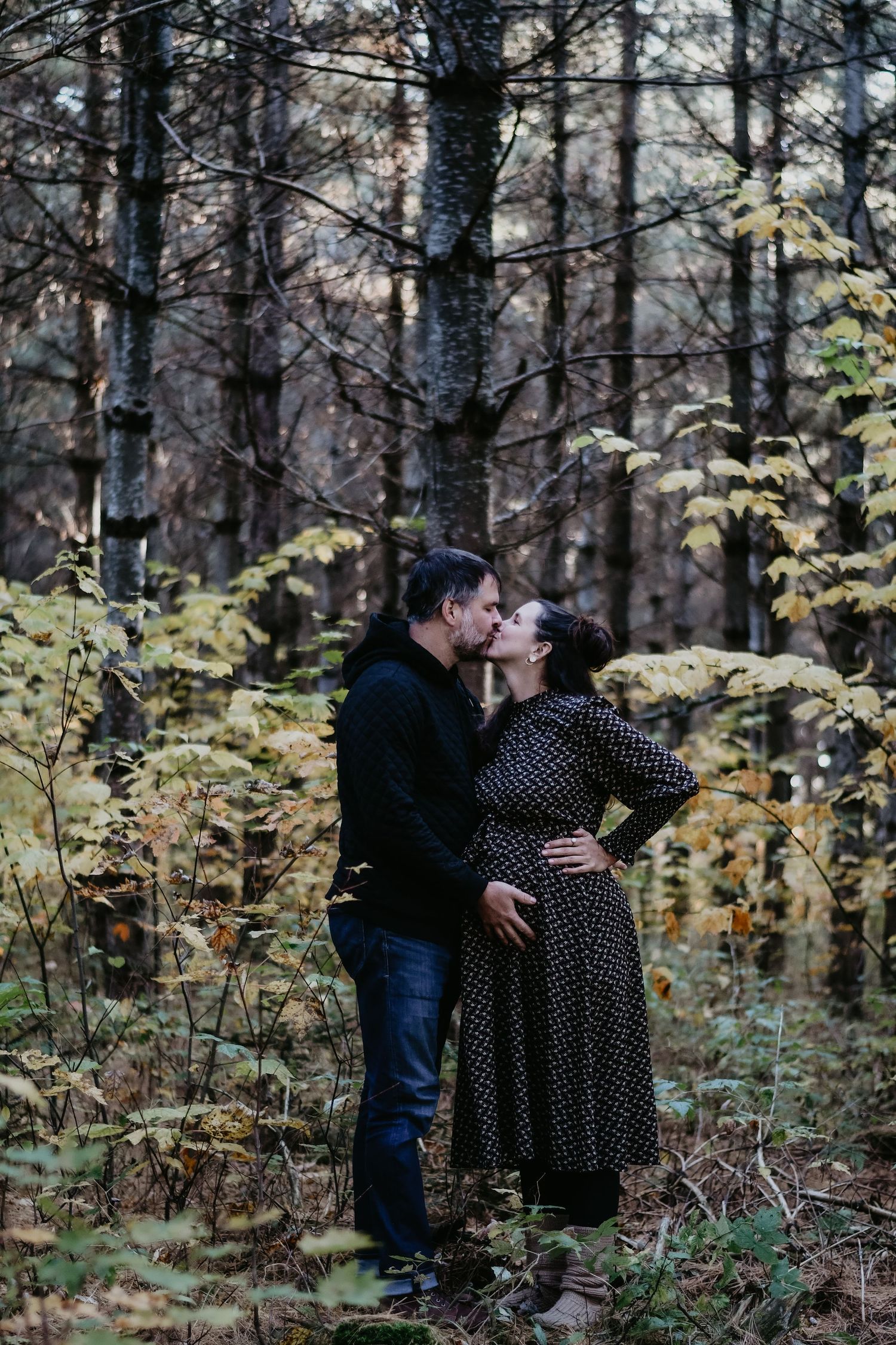 A romantic couple shares a tender kiss among autumn foliage in a forest setting.
