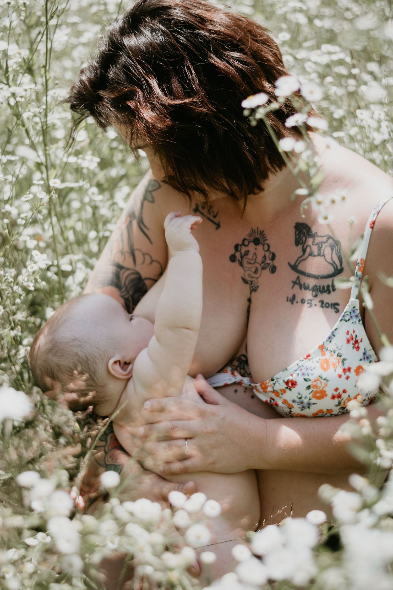 A tender nursing moment captured among white wildflowers, showing tattoos and natural connection.