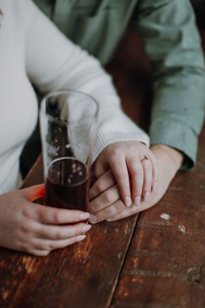 Close-up of hands holding a glass of dark beverage on rustic wooden table.