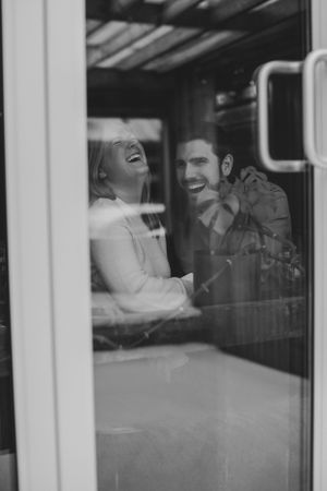 Black and white photo through window showing joyful laughter shared between couple.