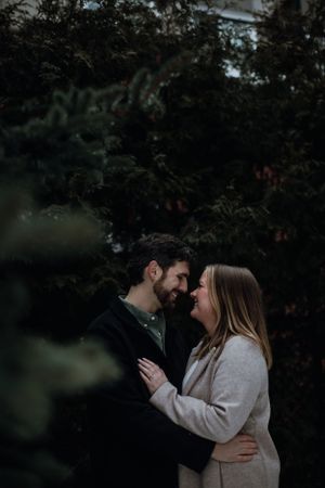 Intimate moment between couple in winter coats against dark foliage background.