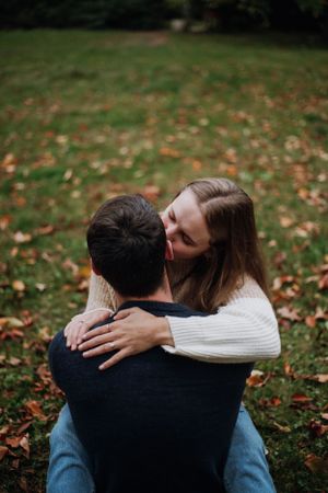 Couple embracing on grass covered with fallen autumn leaves.