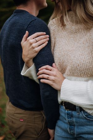 Close-up of hands gently holding onto cozy sweater in autumn setting.