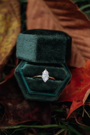 Marquise diamond engagement ring in emerald green velvet box surrounded by autumn leaves.