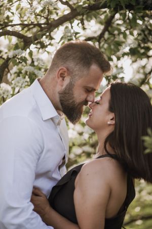 Romantic couple about to kiss under blooming tree branches.