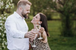 A romantic couple toasts with champagne glasses while sharing an intimate moment in a garden setting.