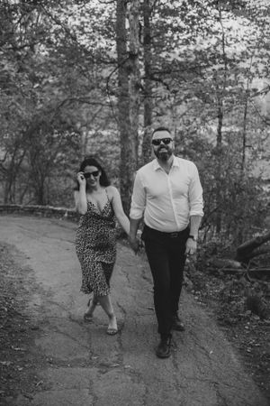 A couple strolls along a forest path in black and white photography.