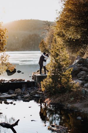Silhouette of a couple embracing on rocks by a scenic lake during golden sunset.