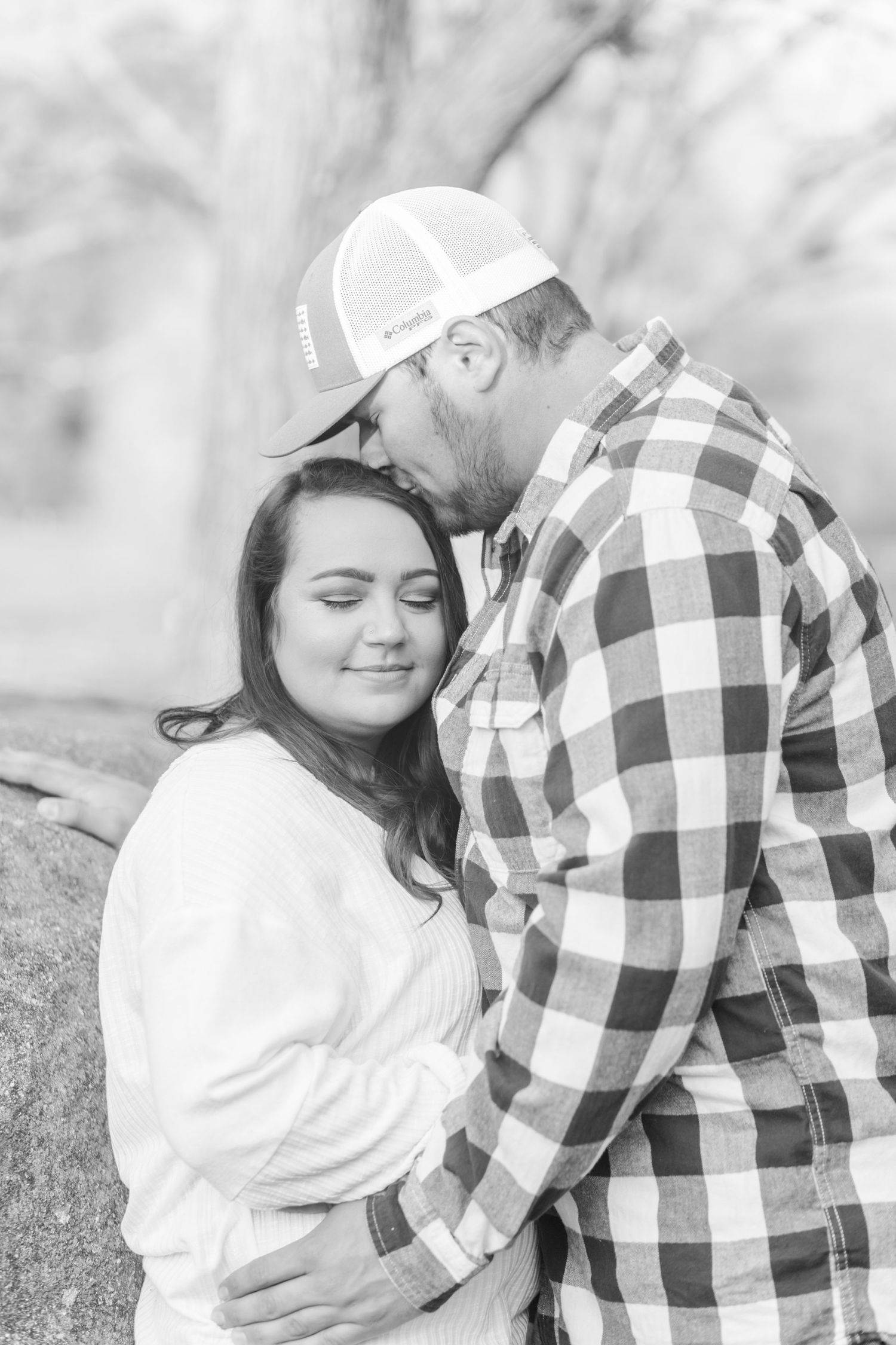 A romantic black and white portrait of a couple embracing against a blurred natural background.