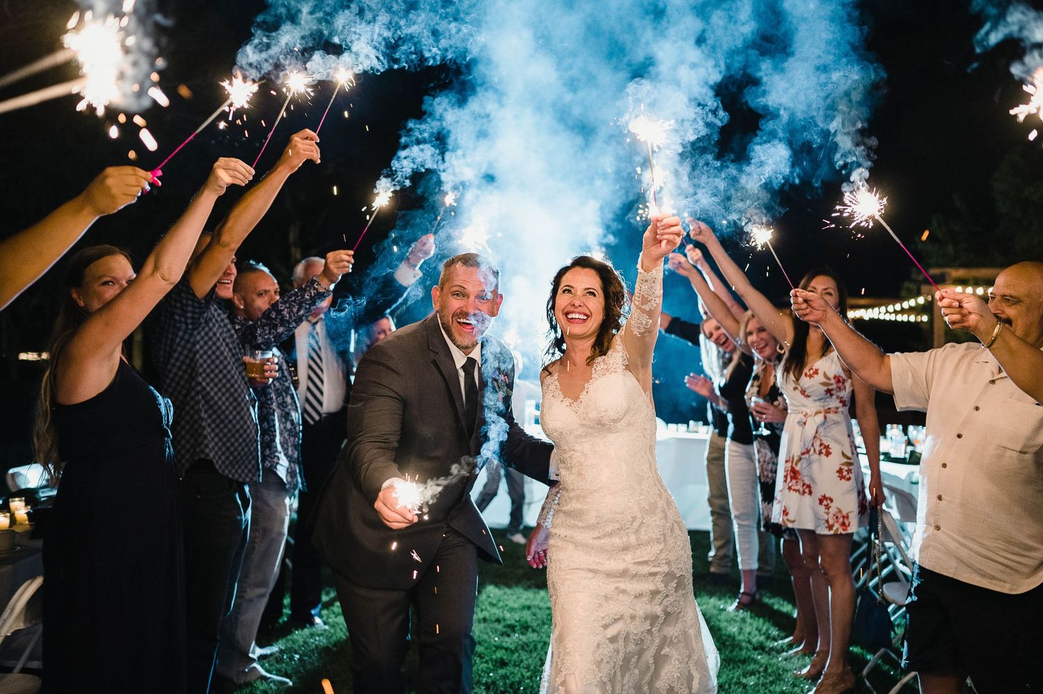 Wedding celebration with sparklers creating blue smoke effects as couple celebrates with guests.