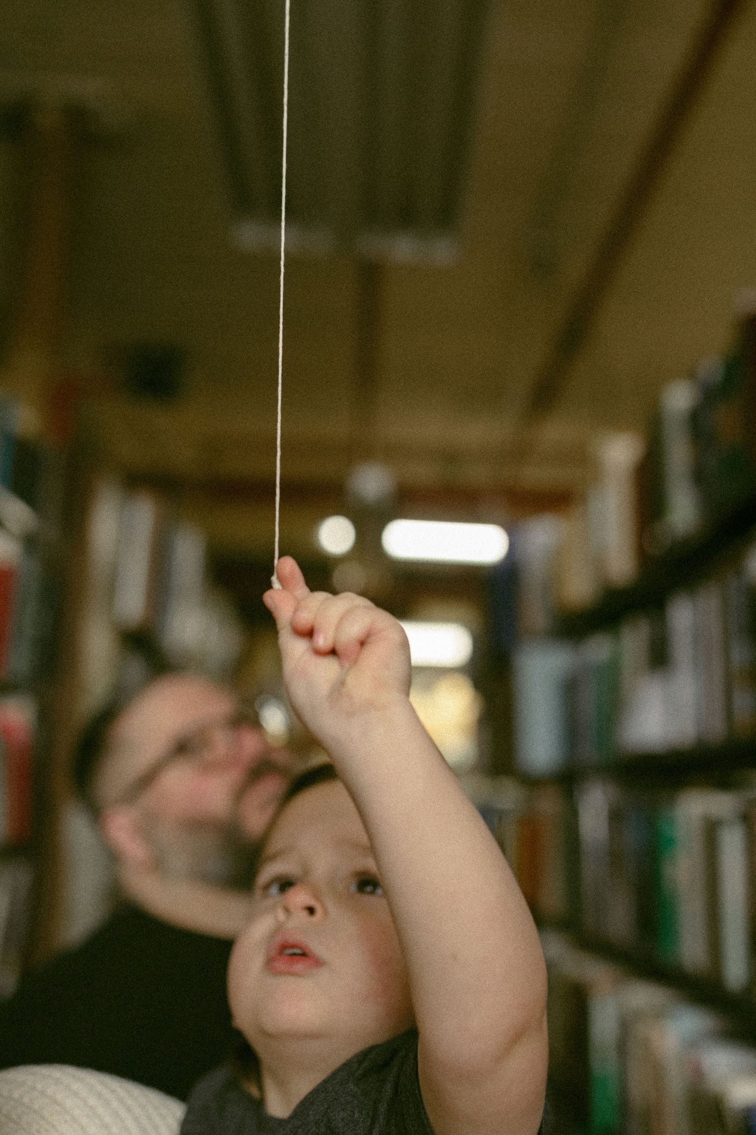 Reaching up towards the library ceiling while exploring book-filled shelves.