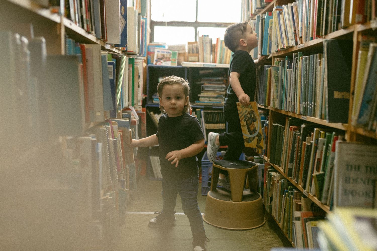 Adventurous browsing between tall library shelves in warm natural lighting.