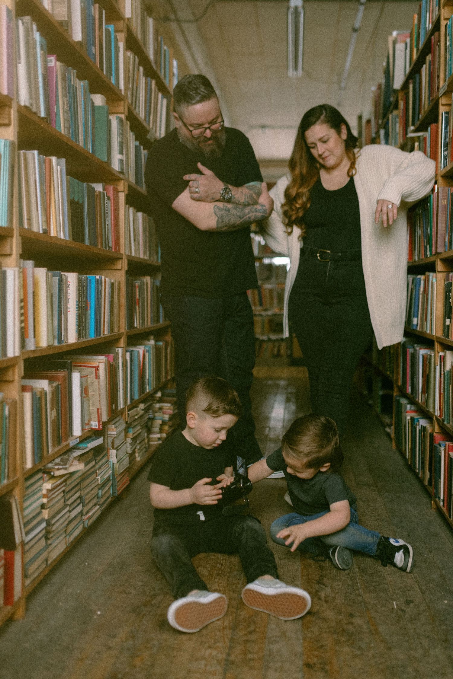 Family group browsing together in a library aisle with children sitting on the wooden floor.
