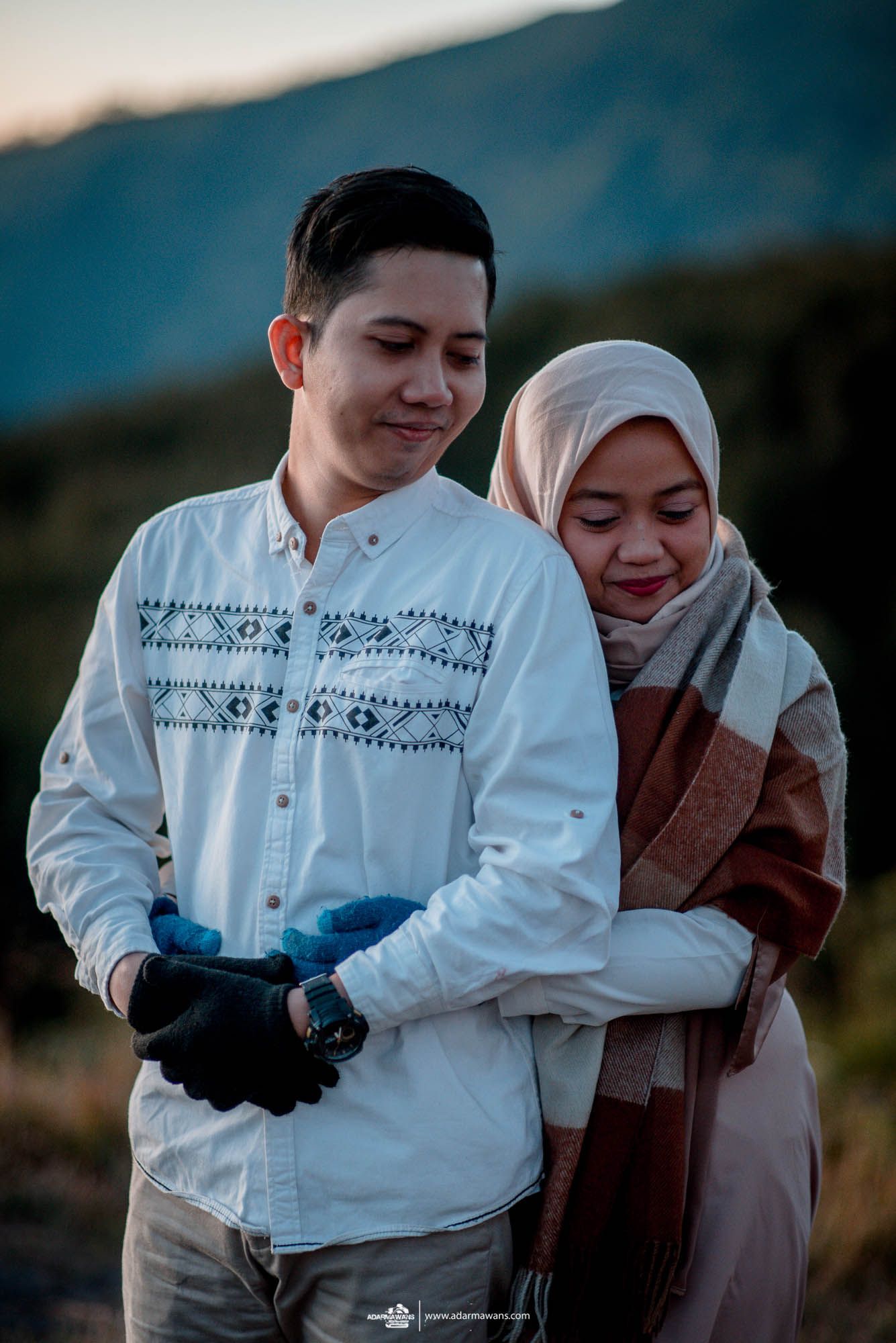 Couple in traditional attire sharing an intimate moment against mountainous backdrop.