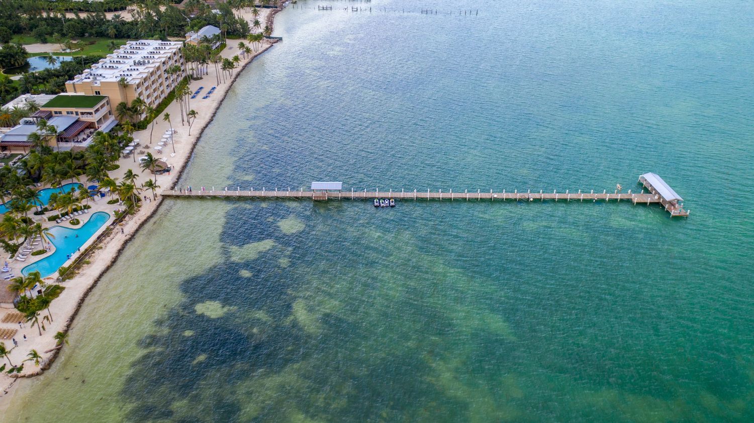 Aerial view of tropical shoreline with pier extending into turquoise waters.