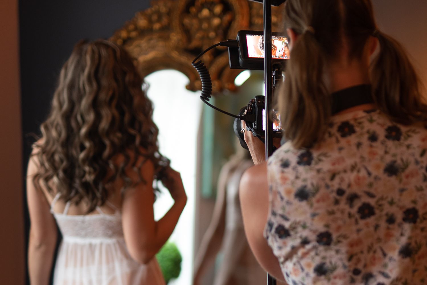 Back shot of videographer and bride facing the mirror