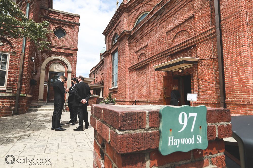 People gathering outside historic church entrance with street number sign.