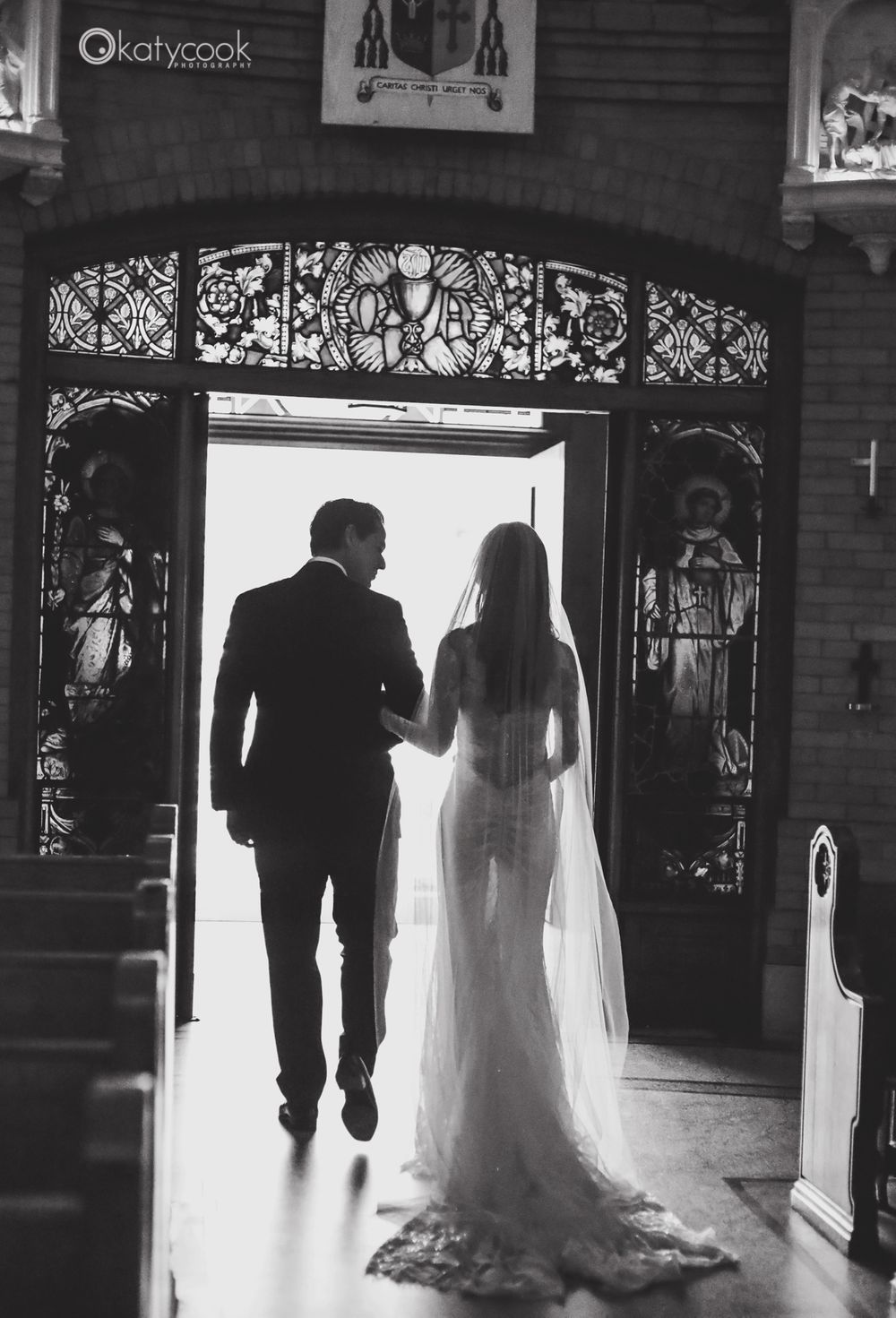 Silhouetted figures walking through ornate church doorway with dramatic backlighting.